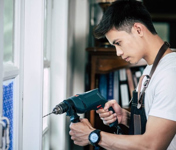 The carpenter holds the drill and drills the window. Selective focus.