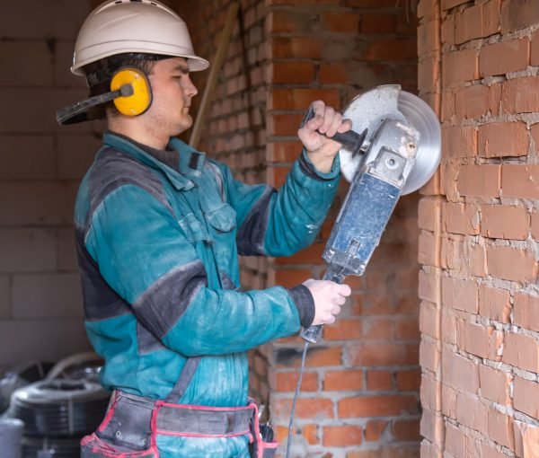 An electrician construction worker in a protective helmet at a work facility works with a grinder.