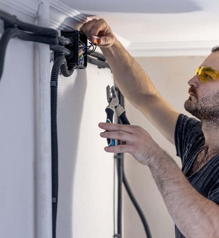 Attractive male electrician repairing an outlet, installing an outlet indoors.