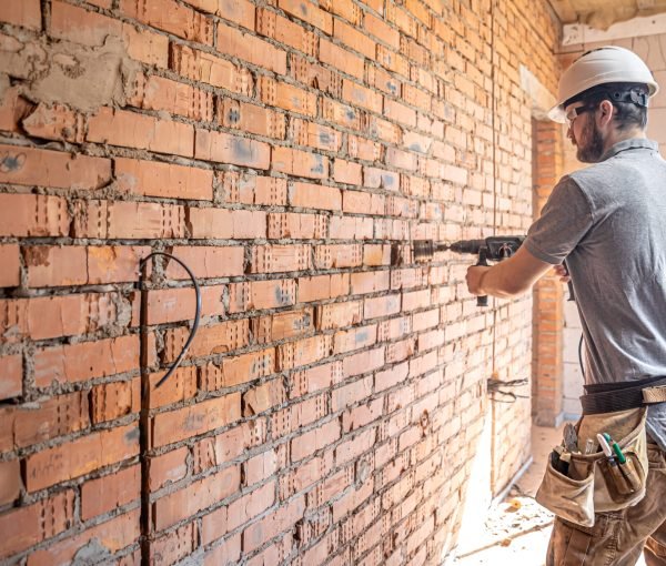Handyman at a construction site in the process of drilling a wall with a perforator.