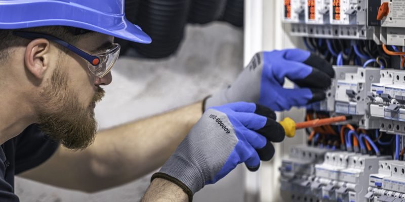A male electrician works in a switchboard with an electrical connecting cable.