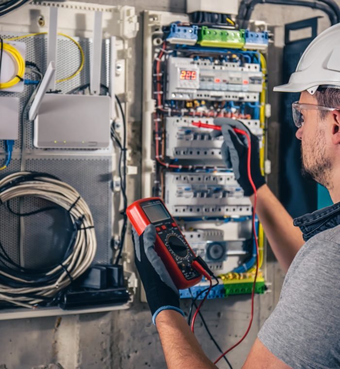 Man, an electrical technician working in a switchboard with fuses. Installation and connection of electrical equipment. Professional uses a tablet.