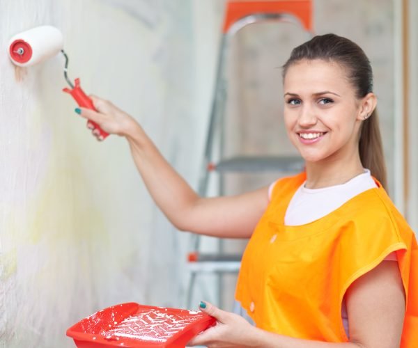 Female house painter paints wall with roller