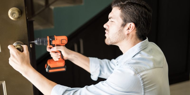 Profile view of an attractive handyman using a power drill to fix a door knob in a house